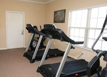 Two treadmills are in a room with a picture on the wall.